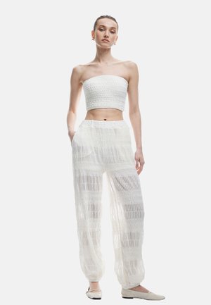 Biały strapless top w stylu crop z fakturowanym marszczeniem, zestawiony z luźnymi, przezroczystymi białymi spodniami z poziomymi paskami i elastycznymi mankietami.