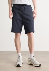 Marinblå shorts med elastisk midja, dragsko och fickor på sidan. Slätt tyg med minimalistisk design och en liten logotypmärke.