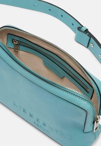 Borsa a tracolla in pelle turchese con cerniera argentata e interno crema. Presenta un compartimento principale e una tasca con zip aggiuntiva per una migliore organizzazione.