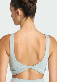 Light blue sports bra with a low back featuring a twisted design, made from smooth, stretchy material, showcasing a minimalist aesthetic.