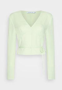Top cropped verde claro com mangas longas, decote em V e detalhe de laço na cintura. Textura suave com costuras destacadas na parte da frente.