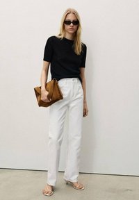Top corto a maniche corte nero lavorato a maglia, pantaloni bianchi a gamba dritta, sandali con tacco rosa chiaro e borsa in suede marrone. Sfondo semplice.