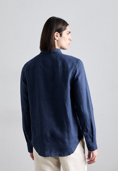 Camisa de lino azul marino de manga larga, con puños abotonados, un collar clásico y un dobladillo curvado. Tela texturizada con detalles mínimos.