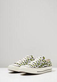 Białe trampki na płaskiej podeszwie z czarnym i neonowo-zielonym printem w panterkę, białe sznurowadła, gumowe podeszwy i klasyczny niski krój.