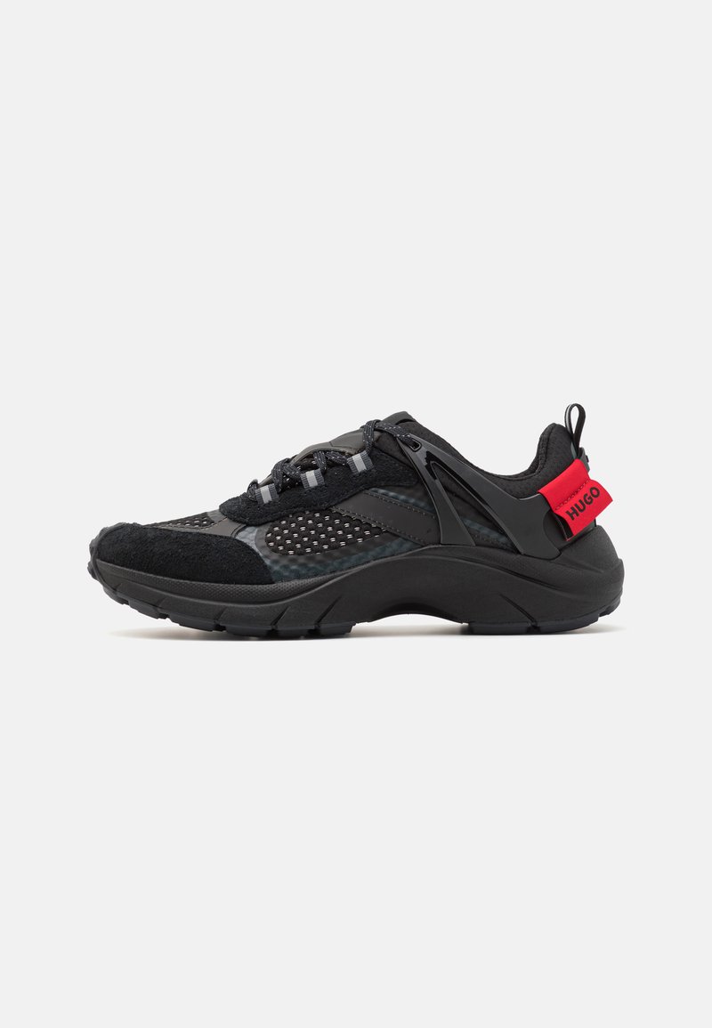 Black athletic shoe featuring mesh and suede materials, a thick sole, curved design, reflective accents, and a red branded heel tab.