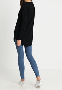 Musta pitkähihainen pusero pyöreällä helmalla, yhdistetty kapealahkeisiin sinisiin farkkuihin ja hopeisiin tennareihin. Rentoon istuvuuteen suunniteltu arkiasu.