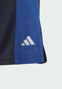 Camiseta deportiva de hombre con un tejido texturizado azul, acentos en negro y un logo blanco de Adidas en la manga. Diseño de manga corta.