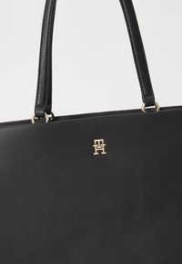 Svart lær tote bag med to håndtak, med en strukturert finish og en gulllogo aksent på fronten.