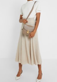 Falda midi beige acanalada combinada con una camiseta blanca de manga corta texturizada; un pequeño bolso cruzado marrón con un cierre dorado acentúa el conjunto.