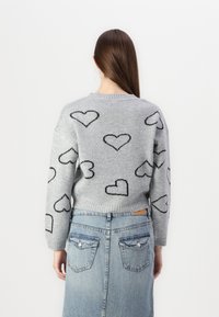 Grå strikkegenser med svarte hjerte mønstre, med en avslappet passform og ribbet kant, kombinert med et høyt midje denim skjørt med lommer.