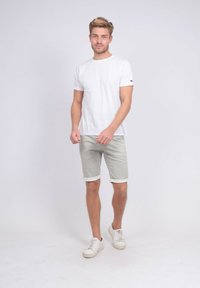 T-shirt blanche col rond associée à un short léger gris clair à revers et des baskets blanches. Design simple avec une coupe droite. Pas de motifs distinctifs.