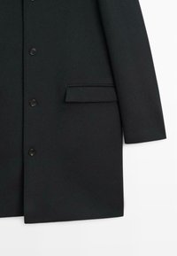 Svart överrock av ett slätt tyg, med knappstängning framtill, en bröstficka och skräddarsydd design med raka linjer.