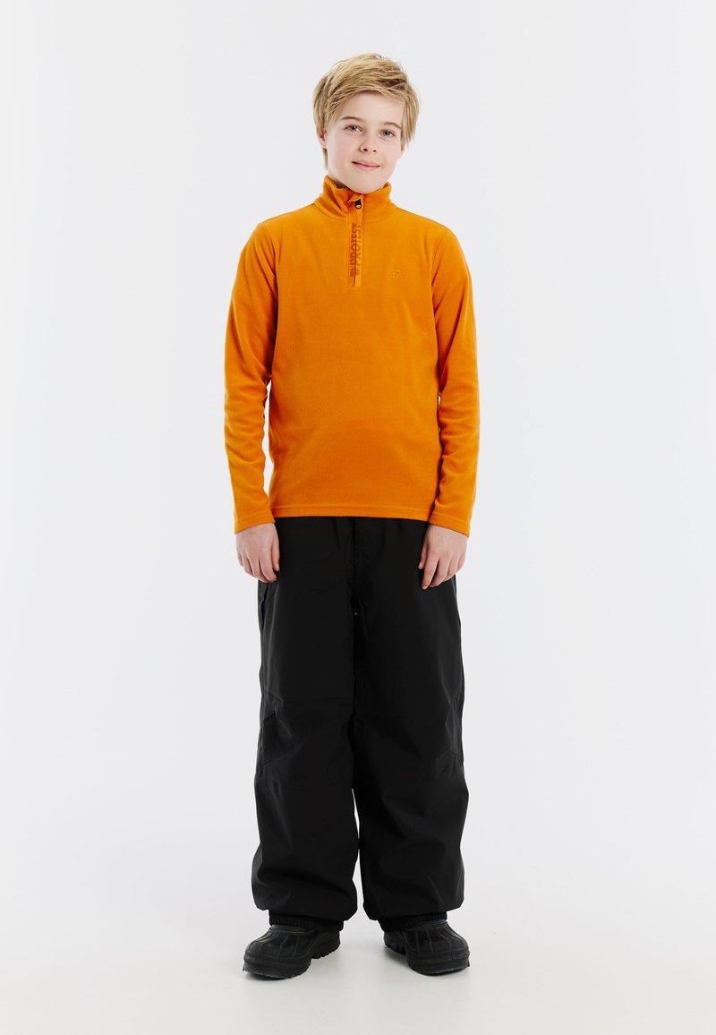 Oranje fleece pullover met hoge kraag en halve rits, gecombineerd met losse zwarte sneeuwbroek en donkere schoenen. Eenvoudig ontwerp, geen patronen.