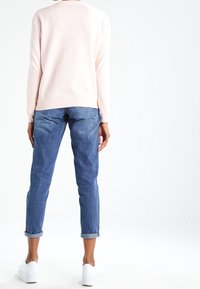 Sudadera de color rosa claro con cuello redondo, combinada con jeans azul enrollados en los puños y zapatillas blancas. El conjunto tiene un ajuste relajado.