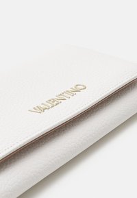 Vit texturerad läderplånbok med en guldprägling av logotypen. Lockdesignen är enkel med en slät inredning.