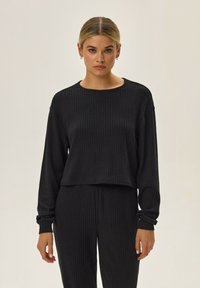 Czarny, prążkowany, długi rękaw top z okrągłym dekoltem i luźnym krojem, uzupełniony teksturowanymi dopasowanymi spodniami o podobnym prążkowanym wzorze.