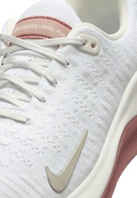 Baskets de course blanches avec une tige en tricot texturé, accents roses et Swoosh beige de Nike. Équipées d'un système de laçage et d'une semelle rembourrée.