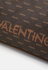 Superficie marrone testurizzata con un logo "VALENTINO" ripetuto in oro metallico, caratterizzato da un logo centrale in grassetto ben visibile. I bordi presentano eleganti accenti dorati.