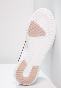 Podešev sportovní obuvi s kontrastní bílou gumovou základnou, texturovaným úchopem a broskvovou akcentací s logem.