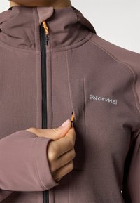 Veste zippée ajustée en mauve, dotée d'une capuche doublée, d'une texture côtelée et d'une tirette orange. Comprend une petite poche zippée.