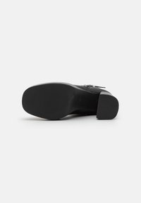 Cizmă cu toc neagră, având un superior din piele netedă, design cu vârf pătrat și talpă exterioară din cauciuc texturat cu caneluri pentru aderență.