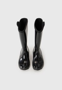 Une paire de bottes en caoutchouc noires brillantes et hautes se tenant debout sur une surface gris clair, vue d'en haut.