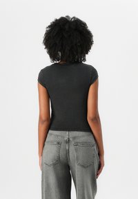Black fitted t-shirt with short sleeves, paired with high-waisted light gray jeans featuring back pockets and a slightly faded texture.