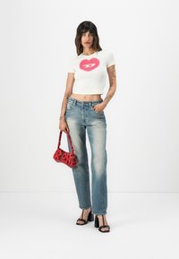 White cropped t-shirt with a pink heart graphic, light blue jeans, red floral handbag, and black chunky heeled sandals.