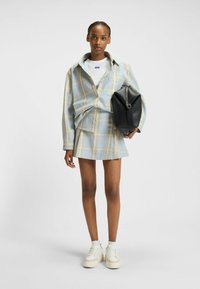 Geruite blouse in lichtblauw en beige, gecombineerd met een bijpassende geruite rok. Witte t-shirt eronder, witte en beige platform sneakers en een zwarte tas.