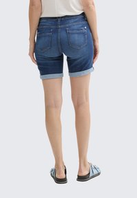 Shorts de mezclilla en azul oscuro con dobladillos enrollados, con un diseño de tiro medio y dos bolsillos traseros. Combinados con zapatillas ligeras de color azul claro.