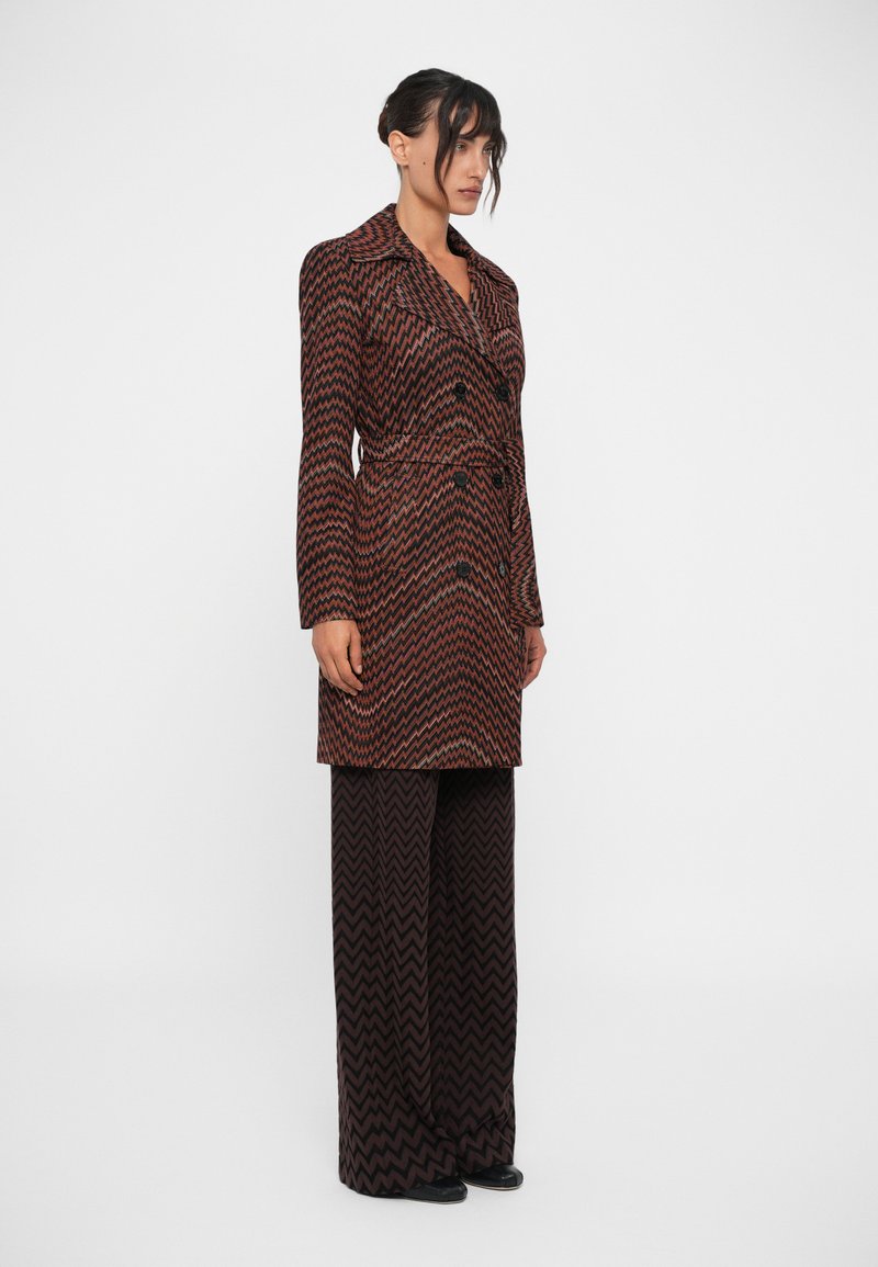 Manteau croisé avec un motif en zigzag vibrant rouge et noir, doté d'un col cranté, de manches longues et d'un design à taille cintrée.