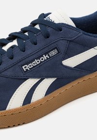 Tengerészkék suéd sneaker fehér bőr kiegészítőkkel és gumírozott talppal. A fűzős kialakítás sötétkék fűzőt és logót tartalmaz.