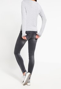 Graues Langarmoberteil kombiniert mit dunkelgrauen Skinny-Jeans. Die Jeans haben eine dezente, verblasste Textur und Gesäßtaschen. Silberne Sneakers vervollständigen den Look.