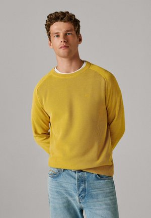 Kollane crew kaelusega pusa tekstuurse kangaga, raglaanvarrukatega ja peene logodetailiga, kombineeritud helesiniste teksadega.