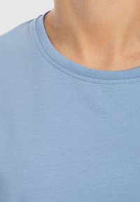 Lyseblå bomulds T-shirt med rund hals og korte ærmer, udstyret med et glat, let struktureret stof og synlige stingdetaljer.