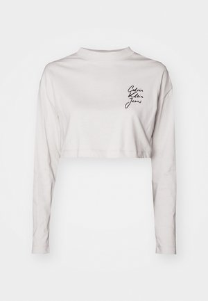 Skraćena majica s dugim rukavima od svijetlosive pamučne tkanine, s visokim ovratnikom i crnim logotipom "Calvin Klein Jeans" na lijevoj strani prsiju.