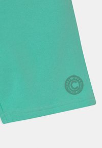 Turquoise athletic shorts with a textured fabric, featuring a circular logo at the hem in a matching matte finish.