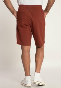 Red shorts with an elastic waistband, featuring two back pockets and a straight cut, paired with white high-top sneakers.