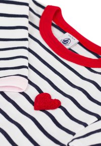 Ριγέ βαμβακερό πουκάμισο με ναυτικό μπλε και λευκές ρίγες, με κόκκινο τελείωμα στο λαιμό και ένα μικρό κόκκινο ταμπελάκι καρδιάς στο μπροστινό μέρος. Απαλά ροζ λεπτομέρειες στα μανίκια.