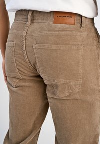 Jasnobrązowe spodnie kordurojowe o żebrowej teksturze, z skórzaną naszywką marki i dwoma tylnymi kieszeniami.