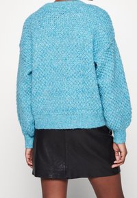 Stickad blå tröja med en texturerad mönstring, rund halsringning och ribbade ärmavslut, kombinerad med en svart läderkjol.