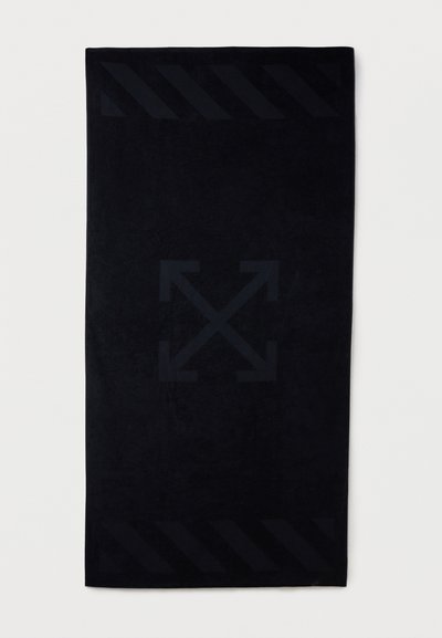 Μαύρη ορθογώνια πετσέτα με διακριτικές ανάγλυφες διαγώνιες ρίγες κοντά στις άκρες και μεγάλο σταυρό με τέσσερα βέλη στο κέντρο.