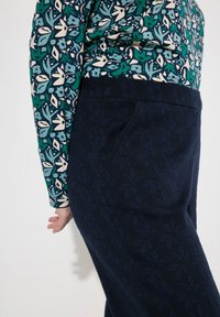 Pitkähihaisessa paidassa on sininen ja vihreä kukkakuosi. Tummansiniset housut, joissa on hienovarainen lehtikuosi ja sivutaskuyksityiskohta.