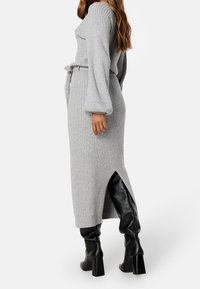 Robe en tricot côtelé gris avec des manches longues et volumineuses, et une ceinture à la taille ; dotée d'une fente latérale et associée à des bottes noires jusqu'aux genoux.