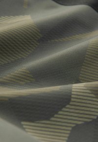 Tessuto testurizzato in verde e beige, caratterizzato da modelli geometrici con strisce e forme di diverse dimensioni, che evidenziano dettagli di design intricati.