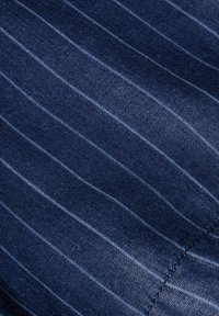 Tessuto blu scuro con sottili righe verticali, realizzato in un materiale morbido e testurizzato. Cuciture visibili lungo un bordo.