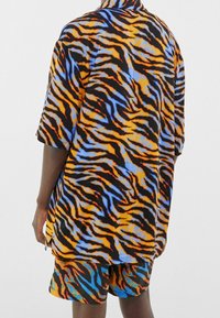 Koszula o luźnym kroju z krótkim rękawem i spodenki wykonane z tkaniny z pomarańczowym, czarnym i niebieskim wzorem w paski tygrysie, o swobodnym fasonie.