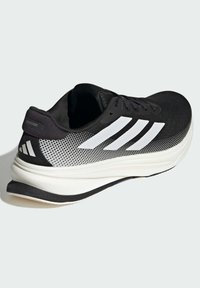 Chaussure de sport noire avec une tige en mesh, des accents rayés blancs et une épaisse semelle intermédiaire blanche. Comprend un col rembourré et une semelle texturée.