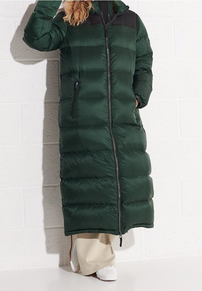 Cappotto imbottito lungo e verde con sezioni trapuntate orizzontali, chiusura con zip, inserti neri sulle spalle e tasche laterali. Texture liscia e lucida.