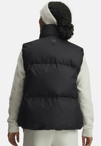 Čierna puff vest, s vysokým golierom, prešívanými sekciami a logom na zadnej strane. Nosená cez svetlý, textúrovaný top.